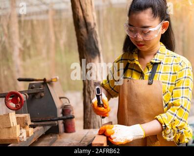 Women standing builder wearing checked shirt worker of construction site hammering nail in the wooden board Stock Photo