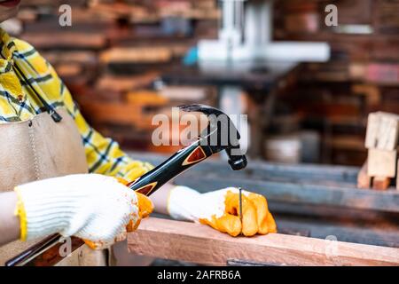 Women standing builder wearing checked shirt worker of construction site hammering nail in the wooden board Stock Photo