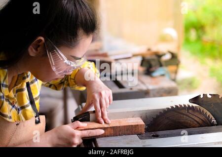Women standing is craft working cut wood at a work bench with circular saws power tools at carpenter machine in the workshop Stock Photo