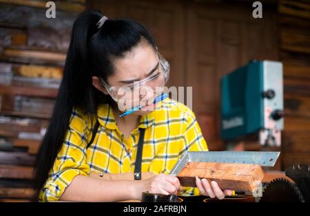 Woman holding ruler and pencil while making marks on the wood at the table in the workshop Stock Photo
