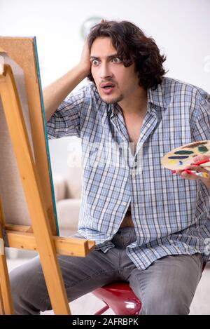 The young handsome man enjoying painting at home Stock Photo