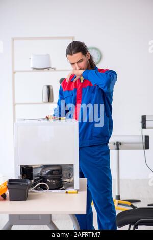 The young male contractor repairing refrigerator at workshop Stock Photo