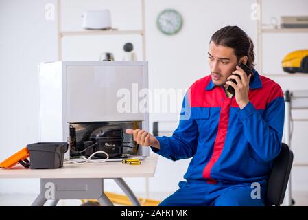 The young male contractor repairing refrigerator at workshop Stock Photo