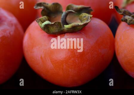 Close-up of orange overripe persimmons lying side by side against dark background