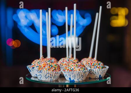 Delicious cake pops, sprinkled with colorful balls, lie on a glass stand. Stock Photo