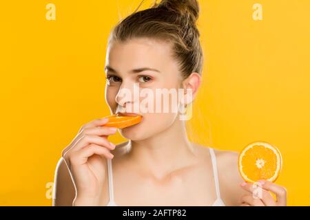Portrait of young beautiful woman eating a orange on yellow background Stock Photo