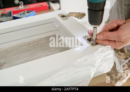 Furniture assembly, close-up screwing chromed door hinges with professional tools Stock Photo