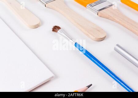 Education art concept. Set of different sizes brushes, blank canvas and various pencils on light background. Drawing supplies. Diagonal layout. Open c Stock Photo