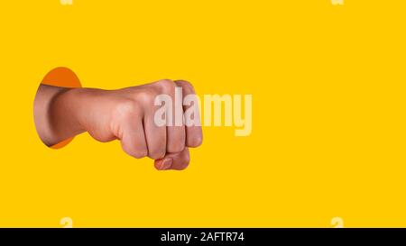 Young womans hand clenched into a fist. Hand sticks out of hole with sharp edges on vibrant yellow background. Equal rights for women concept. Copy sp Stock Photo