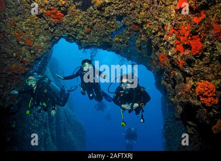 Children scuba diving through a rocky arch overgrown with red sponges, Zakynthos island, Greece Stock Photo