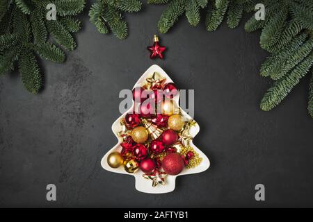 Decorative Christmas tree as plate with red and golden balls on black background. Xmas greeting card. Holiday concept. Happy New Year. View from above Stock Photo