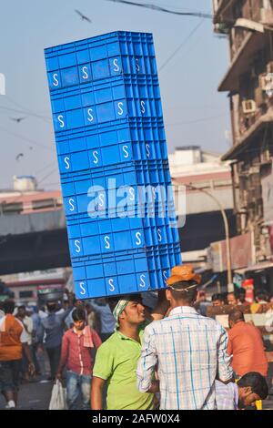 A man working at a fish market next to Crawford Market in Mumbai (Bombay), India, balances half a dozen plastic crates on his head Stock Photo