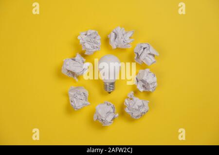 Creativity inspiration, great business idea concept with white light bulb and paper crumpled ball on yellow background. Flat lay, top view, copy space Stock Photo