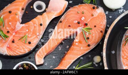 Raw trout fish steaks, pepper and salt, herbs on black stone concrete table, copy space top view Stock Photo