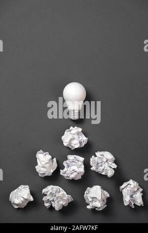 new idea concept with crumpled office paper and white light bulb on grey background. Creative solution during brainstorming session concept. Flat lay, Stock Photo