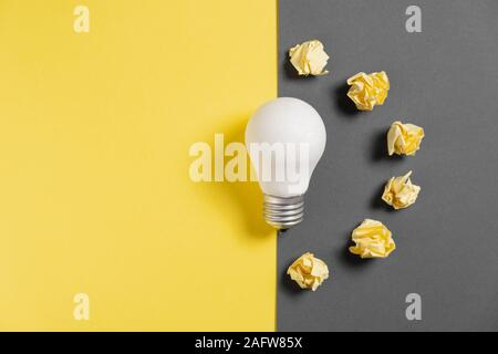 New idea concept with crumpled office paper and white light bulb on black and yellow background. creative solution during brainstorming session. Flat Stock Photo