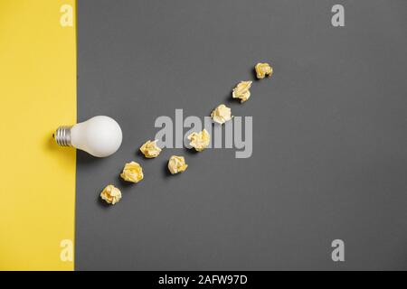 New idea concept with crumpled office paper and white light bulb on black and yellow background. creative solution during brainstorming session. Flat Stock Photo