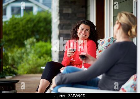 Happy women talking and drinking red wine on front porch Stock Photo