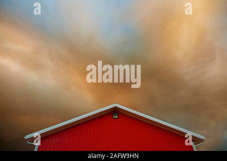 Orange clouds forming in dramatic sky over vibrant red barn Stock Photo