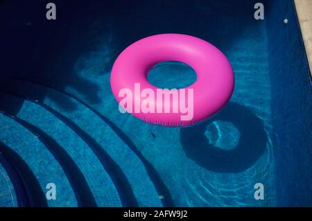 Bright pink inflatable ring in sunny blue swimming pool Stock Photo