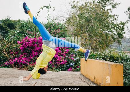 Fit female personal trainer exercising, stretching upside-down in park Stock Photo