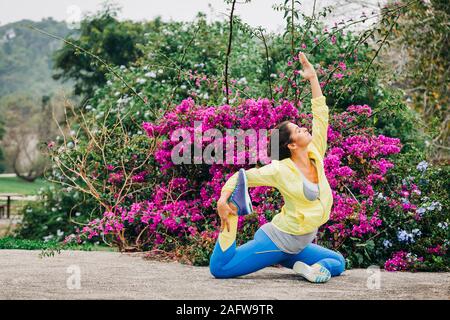 Fit female personal trainer exercising, stretching in park Stock Photo