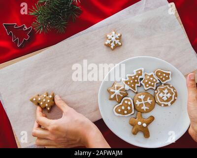 Homemade cookies shaped tree on plate and hand holding Christmas cookies different shapes: star, fir-tree, christmas on white wood background, flat Stock Photo