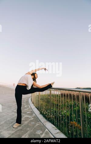 Graceful young female ballet dancer stretching at park railing Stock Photo