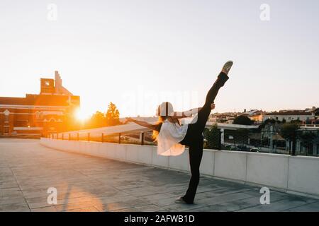 Graceful young female dancer doing standing splits in sunny urban park Stock Photo