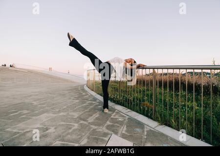 Portrait carefree young female dancer doing standing splits at park railing Stock Photo