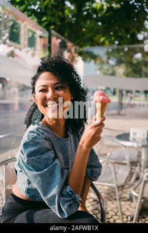 Happy woman eating ice cream cone on sunny cafe patio Stock Photo