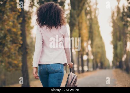 Rear behind view photo of charming dark skin curly lady walking park after college lectures hold backpack returning home autumn season wear jacket Stock Photo