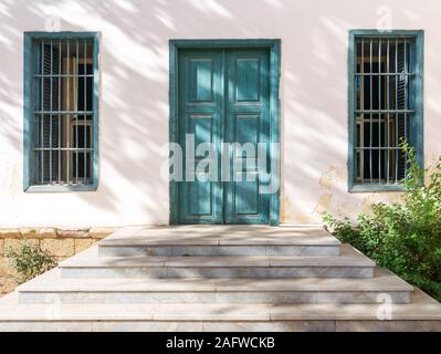 White marble stair in front of white wall with green wooden old grunge decorated door and two wrought iron windows, Old Cairo, Egypt Stock Photo