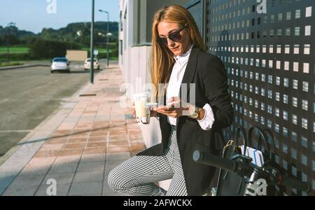 Businesswoman using mobile and drinking coffee with her scooter Stock Photo