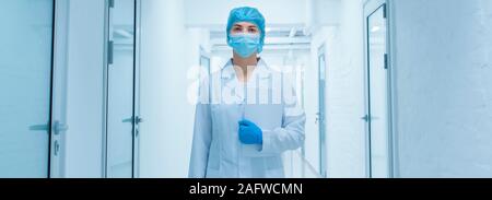 Woman in protective medical wear going through empty laboratory corridor Stock Photo