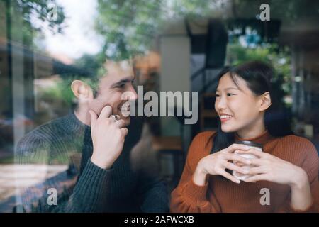 Couple having coffee on a date talking and smile together. shot through window glass Stock Photo