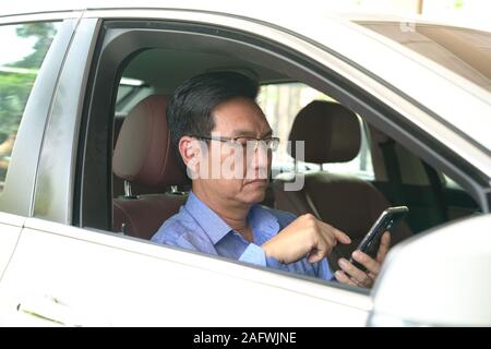 Asian chinese businessman messaging or browsing on his cell phone inside his car Stock Photo