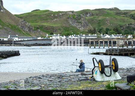 A womand looking back towards the harbour of Ellenabeich, a small village on the isle of Seil  from Easdale Island.  The wheelbarrow in the foreground Stock Photo