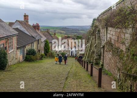 People walking down the steep cobbled street with thatched cottages, Gold Hill, Shaftesbury, Dorset, UK in December Stock Photo