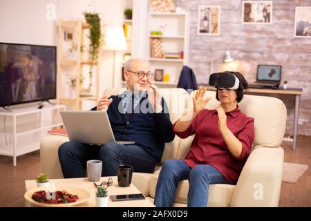 Old elderly retired woman in her 60s experiencing virtual reality for the first time in their cozy apartment Stock Photo