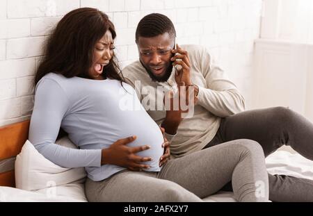 Pregnant woman suffering, husband calling to doctor from home Stock Photo