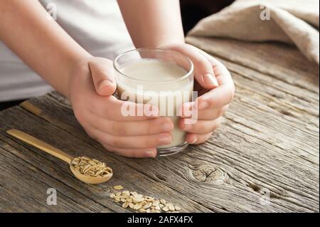 Young adult hands holds drinking glass homemade organic oat milk . Healthy eating lactose free milk substitute concept .Close up,selective focus. Stock Photo