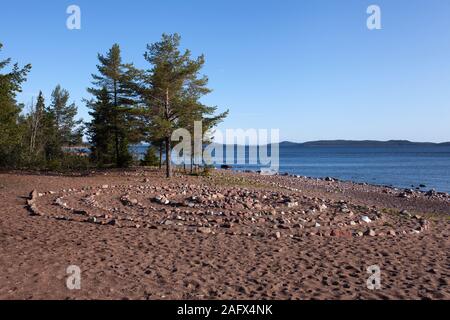 Small labyrinth, maze by the sea. Trees and hills in the background. Sunshine. Stock Photo