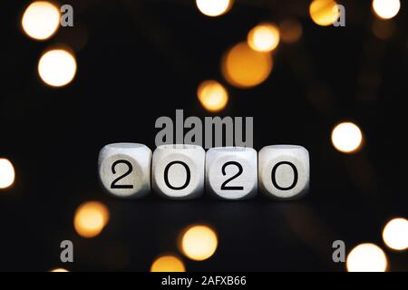 Wooden cubes with 2020 numbers on a black background. Christmas concept greeting card with blurred bokeh lights. Stock Photo