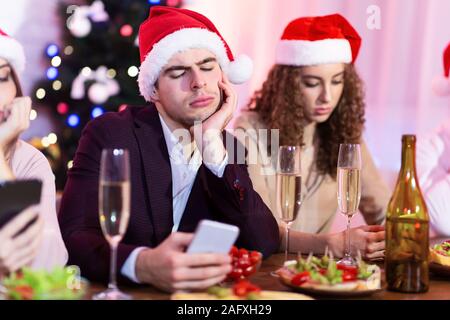 Bored Couple Using Phones During New Year Celebration Sitting Indoor Stock Photo