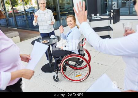 Business team colleague waving woman in wheelchair for greeting and inclusion Stock Photo