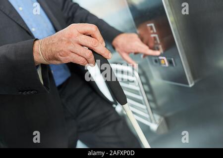 Blind man with cane presses button in elevator of business office Stock Photo