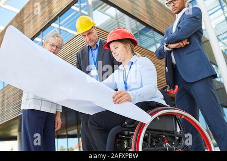 Disabled woman as an architect in a wheelchair with blueprint together with engineers Stock Photo