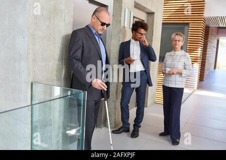 Blind man with a cane and business colleagues waiting in front of the elevator Stock Photo