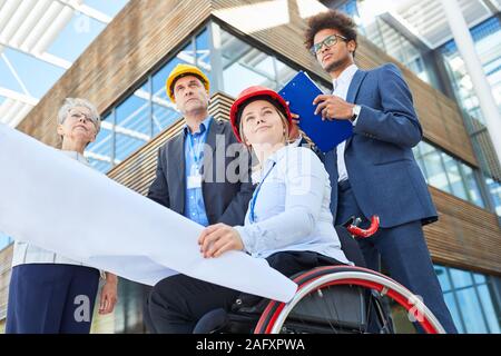 Woman as an architect in a wheelchair with blueprint next to engineers for an office Stock Photo